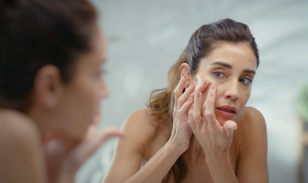 Frau begutachtet ihr Gesicht kritisch im Spiegel