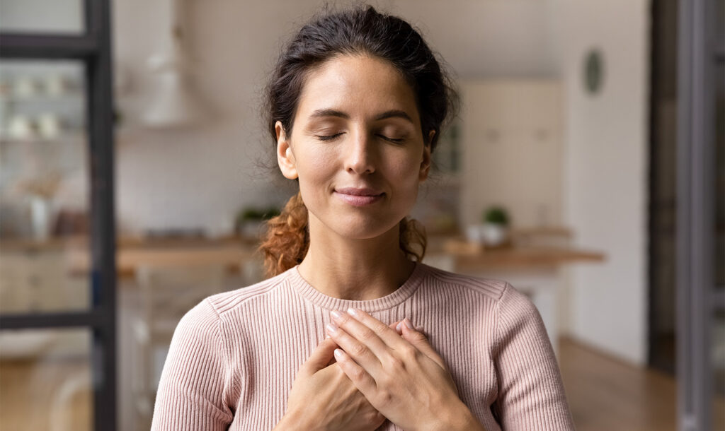 Lächelnde Frau mit geschlossenen Augen und ihren Händen über der Brust